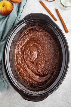 an overhead view of a chocolate cake in a bowl with cinnamon sticks and apples around it