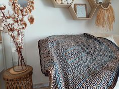 a bed covered in a blue and white blanket next to a vase with dried flowers