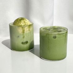 two glasses filled with green liquid sitting next to each other on a white counter top