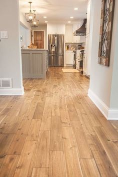 an empty kitchen and living room with wood flooring in the center, along with stainless steel appliances