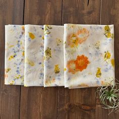 four napkins with flowers on them sitting on top of a wooden table next to a plant