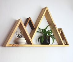 three wooden shelves with plants and vases on each shelf in front of a white wall