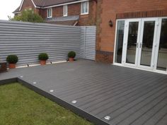 a deck with potted plants on it next to a brick wall and sliding glass doors