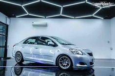 a silver car parked in front of a white wall with lights on it's sides