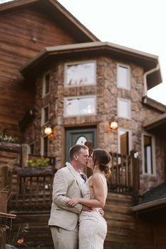 a bride and groom kissing in front of a large wooden house with stone sidings