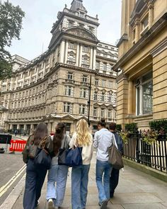 four people walking down the sidewalk in front of buildings