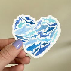 a hand holding up a heart shaped sticker with blue and white designs on it