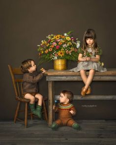 two children sitting at a table with flowers in front of them and one child eating