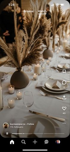 the table is set with white plates, silverware and tall pamphinias