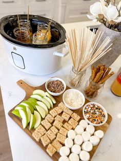 an assortment of food is displayed on a table with a crock pot and utensils