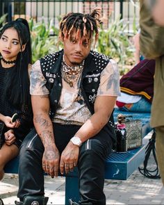 two people sitting on a bench in front of some plants and one person with dreadlocks