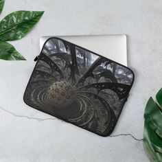 a laptop case with an abstract design on it and green leaves around it, sitting on a white surface