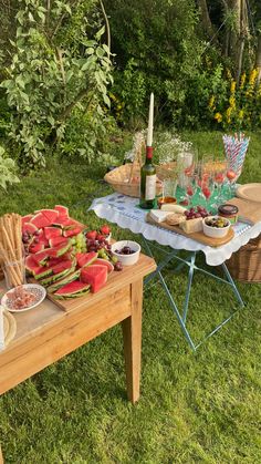 a picnic table with food and drinks on it in the grass next to some trees