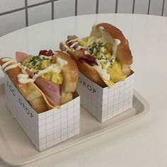 two hot dogs with toppings sitting on a white tray in front of a tiled wall