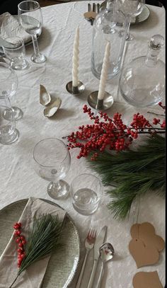 the table is set for christmas dinner with silverware and red berries on top of it