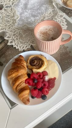 croissants and berries on a white plate next to a cup of coffee