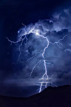 a black and white photo of lightning striking through the sky over mountains with dark clouds