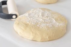 two uncooked doughnuts sitting on top of a white surface next to a rolling pin