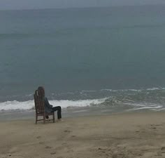 a person sitting in a chair on the beach looking out at the water and waves