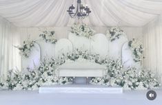 a white couch sitting under a chandelier covered in flowers and greenery on top of a stage