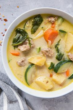 a white bowl filled with meat and vegetable soup on top of a gray table cloth