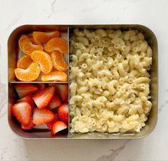 an open lunch box with macaroni, oranges and strawberries