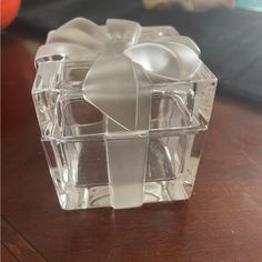 a clear glass box with a bow on the top sitting on a wooden table next to an orange