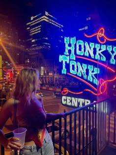 a woman standing on a balcony next to a neon sign that reads honky tonks center