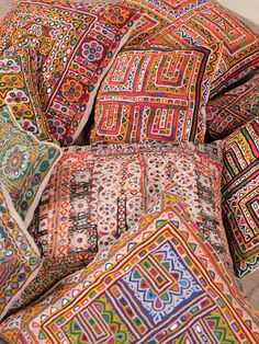 a pile of colorful pillows sitting on top of a bed