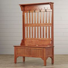 an antique wooden bench with coat hooks on the top and bottom shelf, in front of a white brick wall