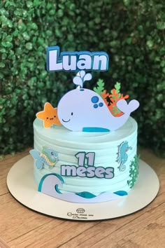 a blue and white whale themed birthday cake on a table with greenery in the background