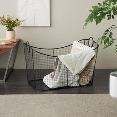 a black wire basket with towels and blankets on it next to a potted plant