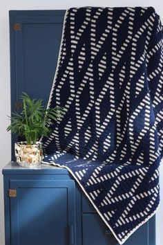 a crocheted blanket sitting on top of a blue cabinet next to a potted plant