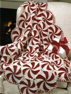 a red and white crocheted blanket with a bow on it next to a fireplace