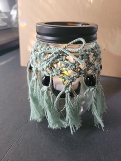 a crocheted candle holder with beads and tassels on the handle is sitting on a table