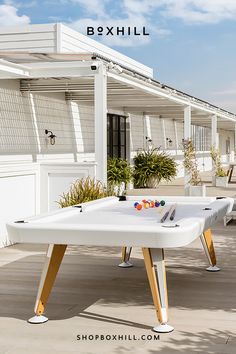 A white rectangular outdoor pool table set on a wooden deck outdoor patio with several potted plants American Pool Table, Outdoor Pool Furniture, Outdoor Pool Table, Resin Wicker Patio Furniture, Outdoor Fireplace Designs, Tennis Table, Expandable Dining Table, Outdoor Table Lamps