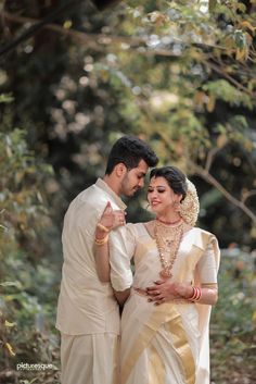 a man and woman standing next to each other in front of some trees with their arms around each other