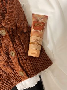 a tube of sunscreen sitting on top of a bed next to a brown sweater