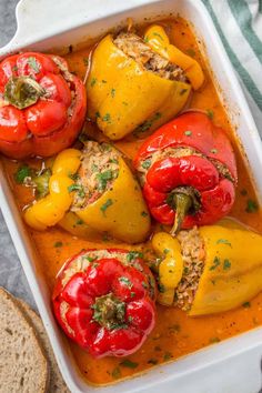 stuffed bell peppers in a white casserole dish with bread and napkin on the side