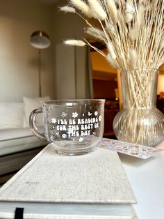 a glass cup sitting on top of a table next to a vase