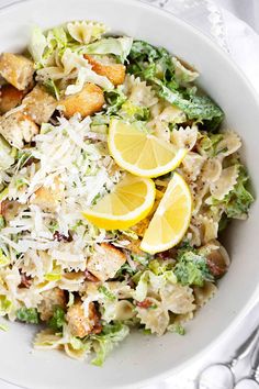 a white bowl filled with pasta salad and lemon wedges