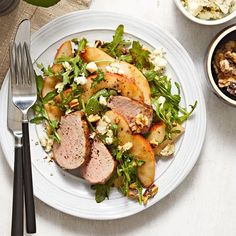 a white plate topped with meat and vegetables next to a bowl of salad on a table