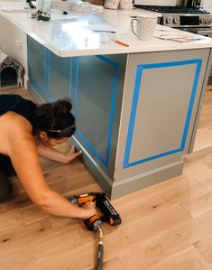 a woman working on a cabinet in a kitchen with blue trimmings and tools