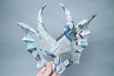 a person holding up a paper origami bird made out of newspaper strips and magazines