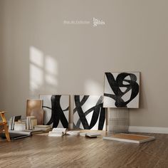 three black and white paintings are on the wall next to a wooden table with books