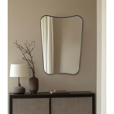 a mirror on the wall above a dresser with a lamp and vase in front of it