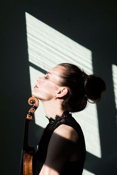 a woman holding a violin in her right hand and looking up at the sun coming through the window