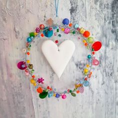 a white heart shaped ornament hanging from a chain with colorful beads and charms