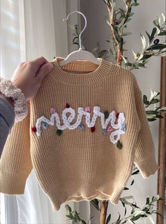 someone is holding up a sweater with the word merry written on it in white letters