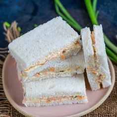 three sandwiches stacked on top of each other on a pink plate next to green onions